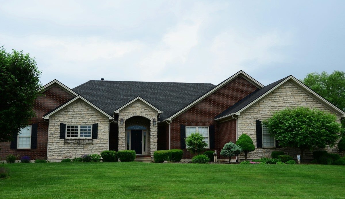 A brick and stone house with a dark shingle roof and a wide lawn