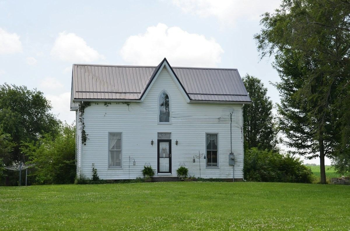 A white farmhouse with a gray metal roof and a dormer