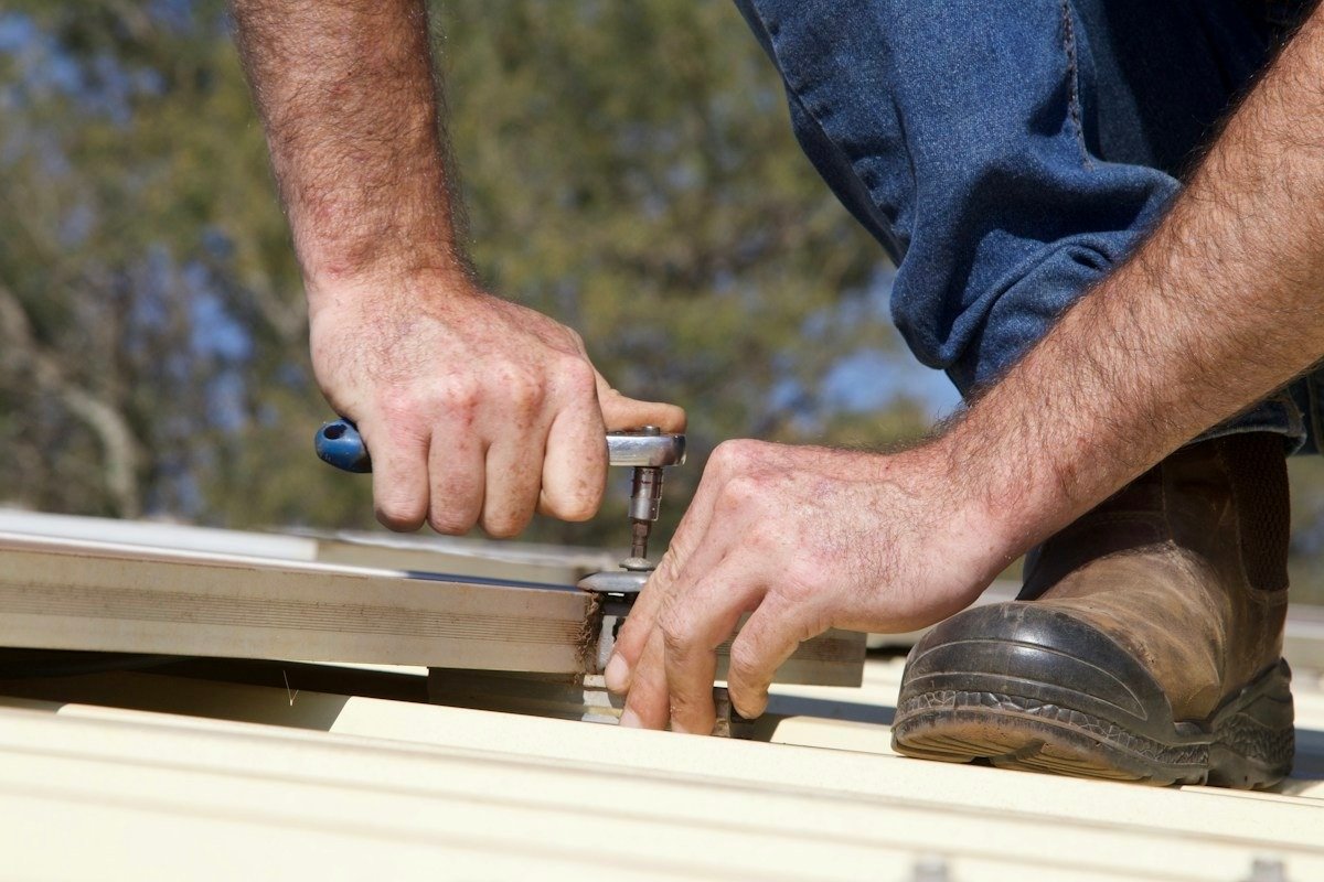 A worker fastening a metal roof panel with a ratchet