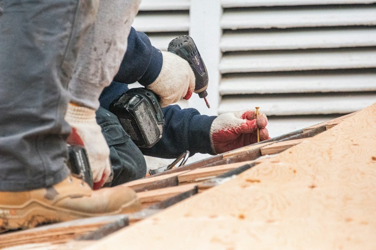 Gloved hands driving screws into new plywood roof decking
