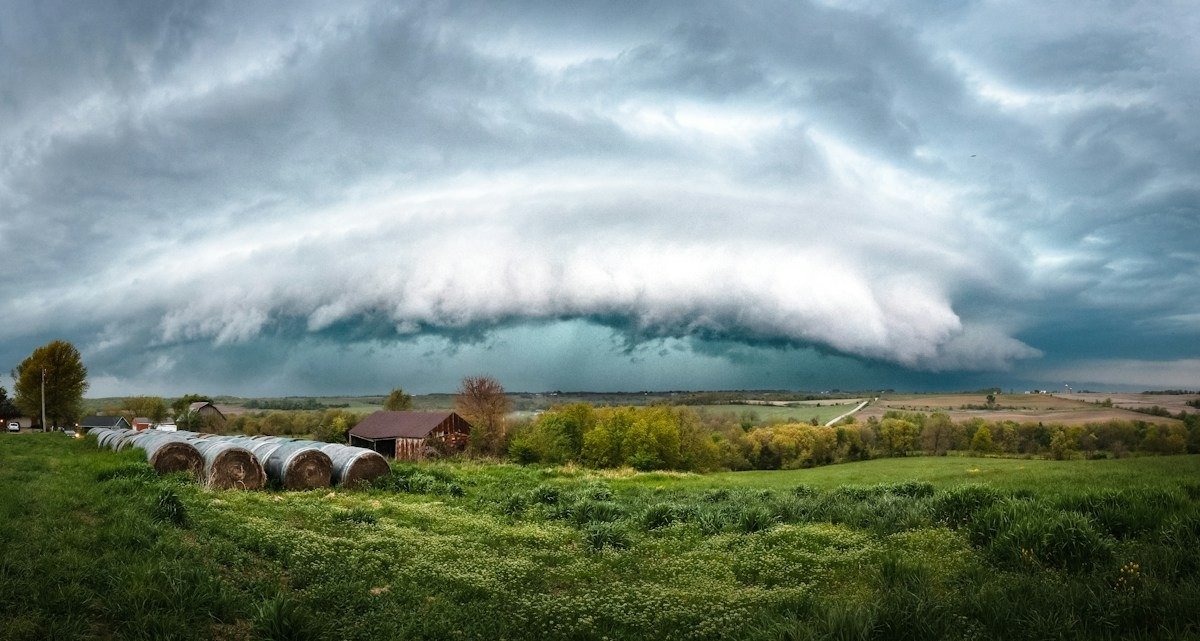 A shelf cloud rolling over farmland with round hay bales