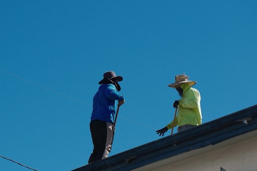 Two roofers in wide-brim hats standing on a roof ridge under a clear sky